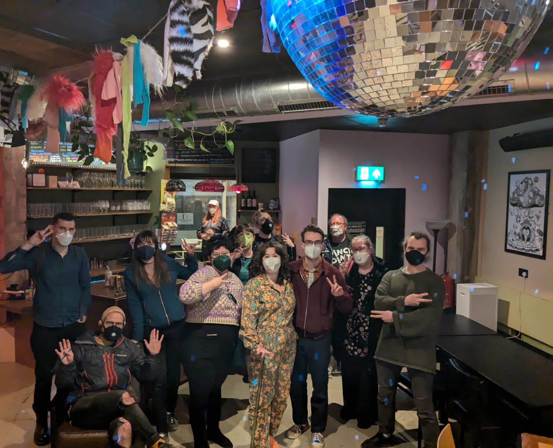 A group of masked people in a bar pose for a photo, with bunting and a disco ball above