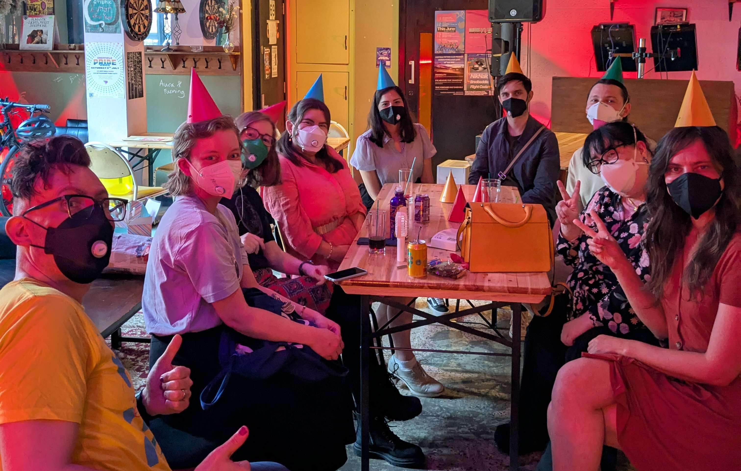 Birthday party A group of masked people in party hats sitting around a table with lots of decorations surrounding them