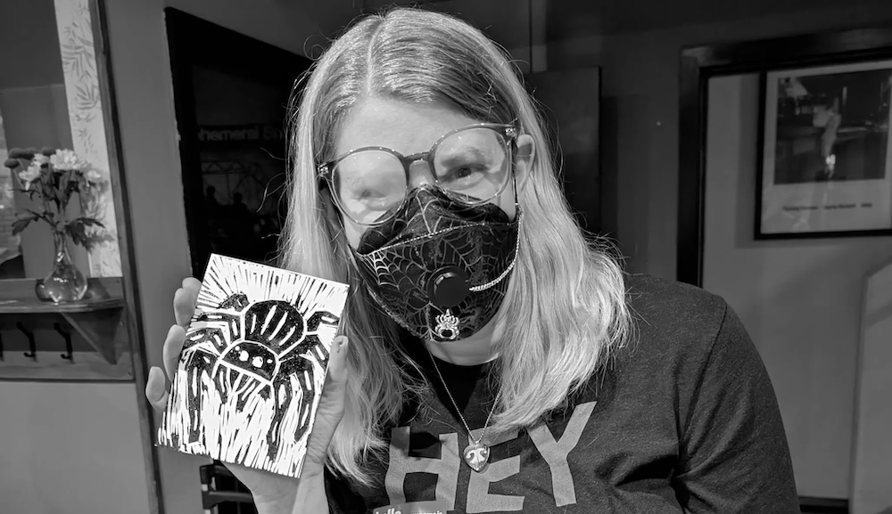 Halloween social A person in a mask holding a lino cut of a spider